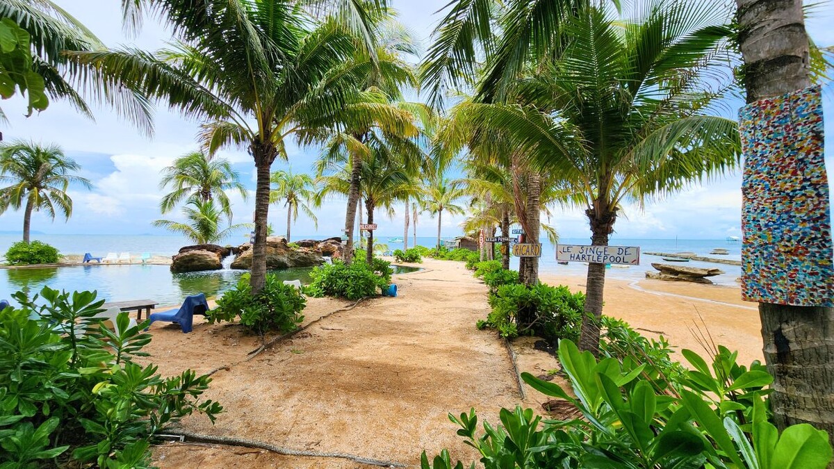 Sandy path lined with palm trees and quirky hand-painted signs leading to a rock pool and the sea at Rory's Beach Bar, Phu Quoc