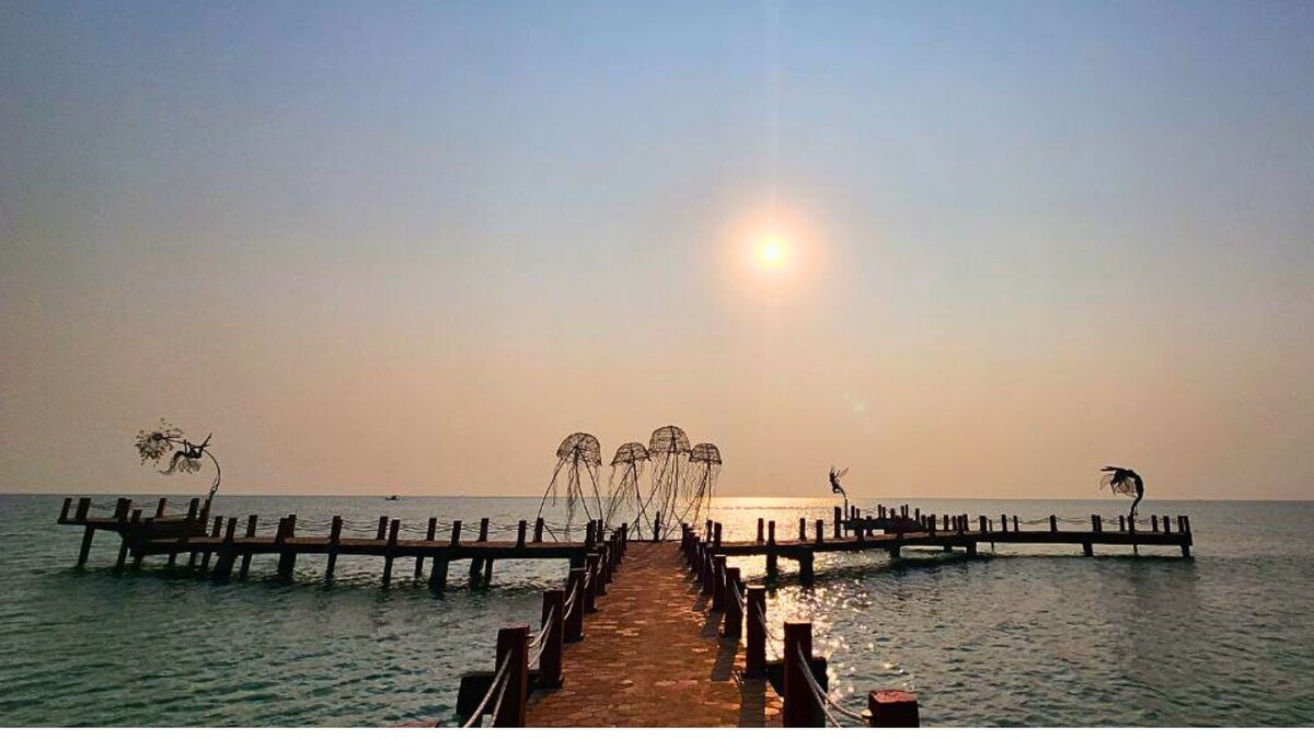 Wooden boardwalk extending into the sea lined with wire jellyfish sculptures and flying-figure statues at sunset at Sanato Beach, Phu Quoc