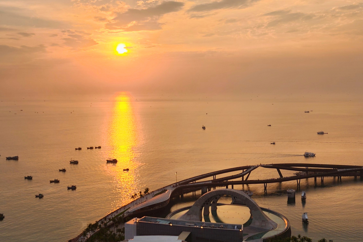 Aerial sunset view of Kiss Bridge's circular amphitheater structure over the sea with fishing boats at Sunset Town, Phu Quoc